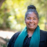 Wendy Jackson outside at Westmont smiling wearing a blue scarf and black shirt with her hair in a bun